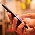 a pair of hands hold a mobile phone; the index finger of one hand is touching the screen