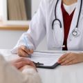 A doctor filling out a form sitting across from a patient. 
